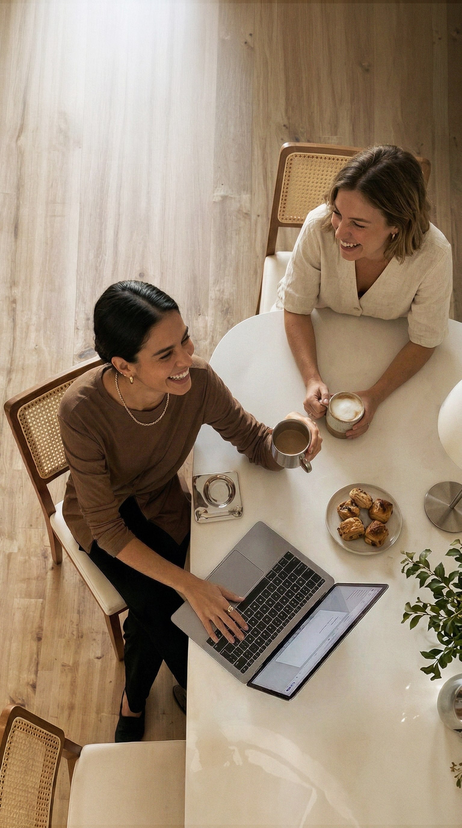 Duas mulheres conversando à mesa com café e um notebook